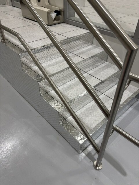 Stainless steel stair handrail over access floor steps with diamond plate nosings at Photonics, Vancouver